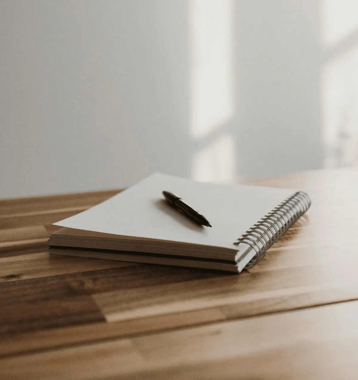 A notebook with a pen on top of a wooden table